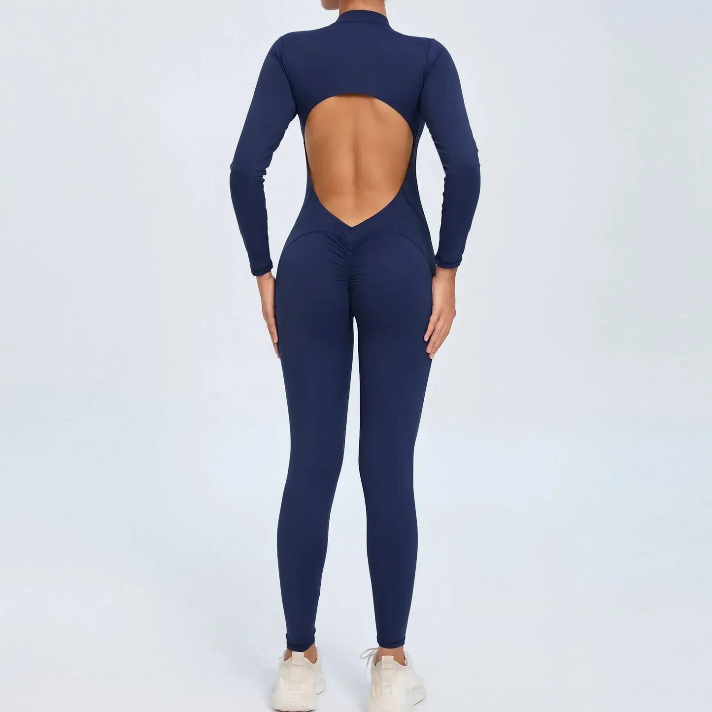Model wearing navy blue women’s open back workout jumpsuit, seamless V-back one-piece