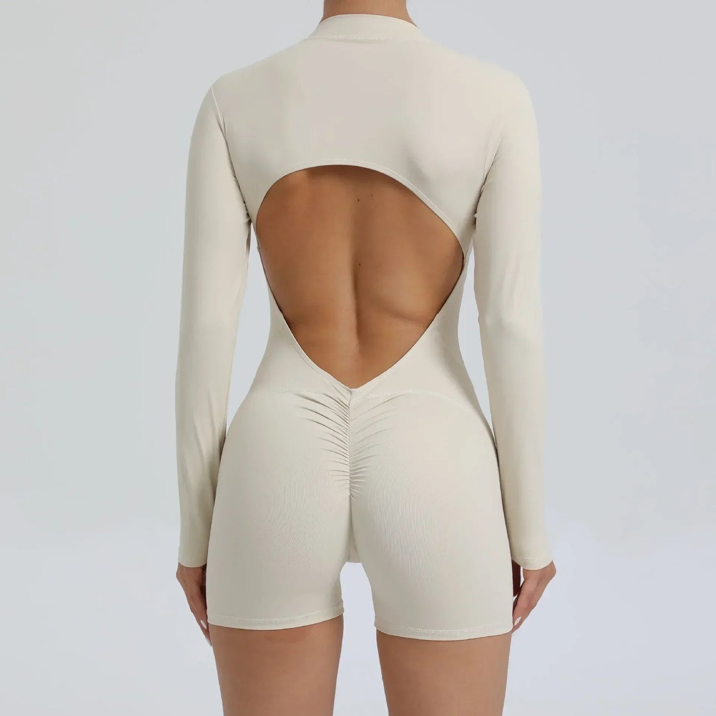 Model wearing beige women’s open back workout jumpsuit, seamless V-back one-piece
