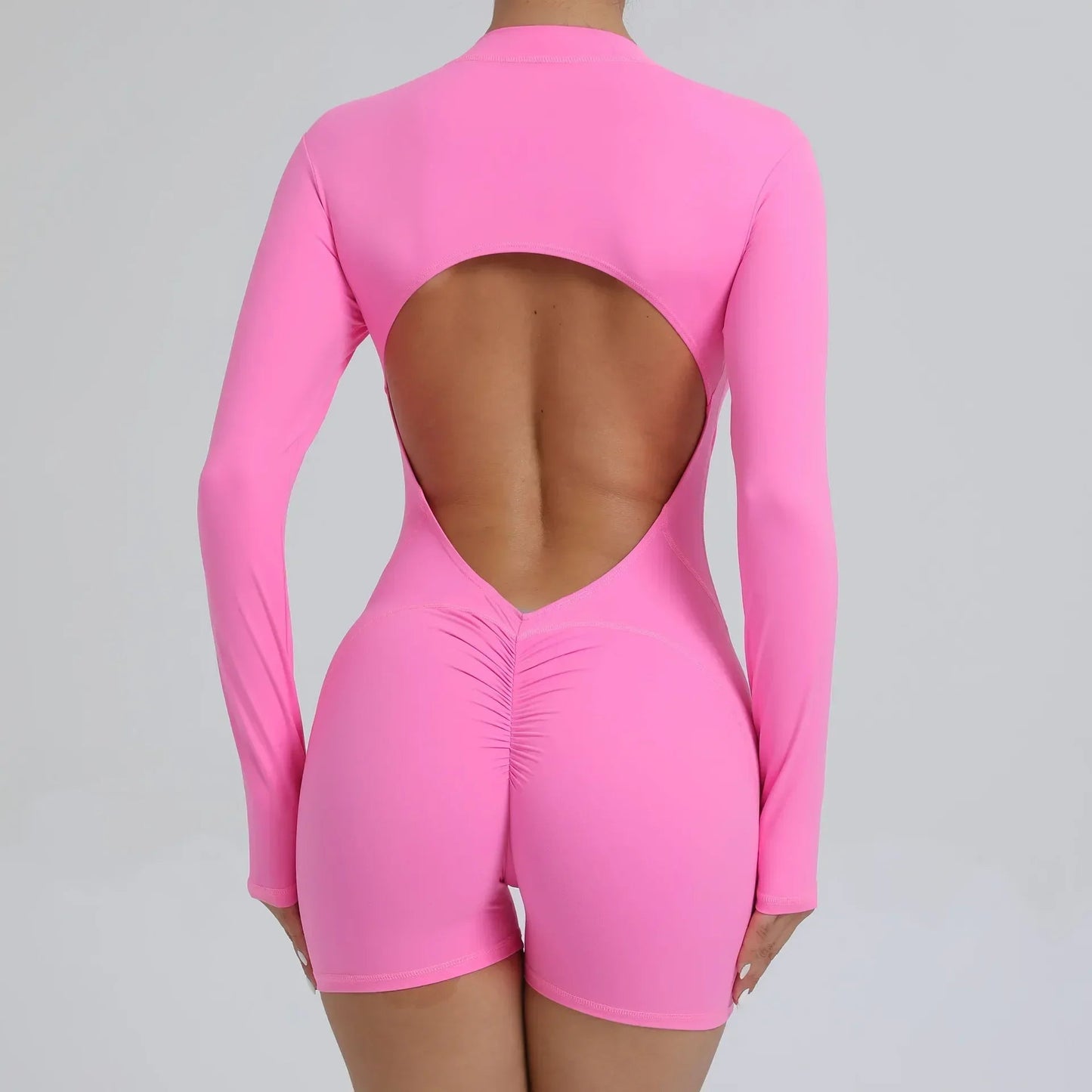 Model wearing pink women’s open back workout jumpsuit, seamless V-back one-piece